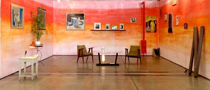 Contemporary art gallery installation in LIAA Project space “Malonioji 6”, featuring abstract sculptures by Landzbergas and vibrant paintings by Axel Linderholm on sunset coloured walls. It gives the impression of a cozy living room.