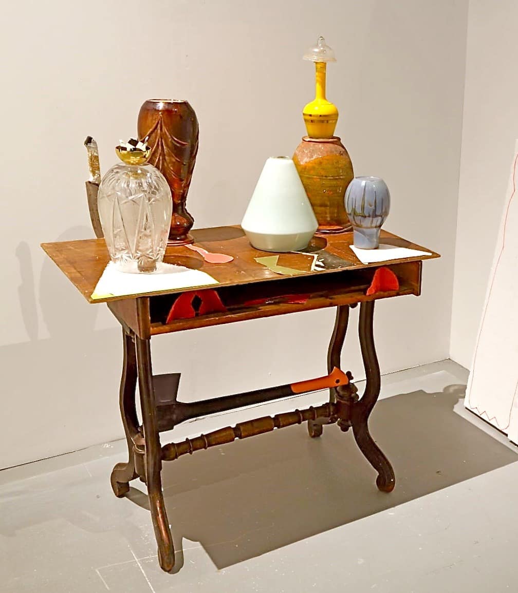 Art installation featuring a table with pottery, utensils and sculptures in the Centre for Contemporary Art Vilnius. Under the table top an axe is installed, which gives a sense of unease.